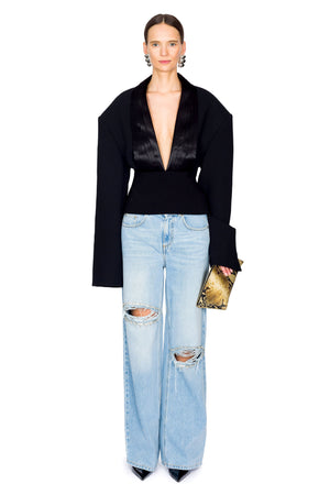 Woman wearing a black long sleeve top with deep v-neck and light blue jeans with distressing and crystals on a white background