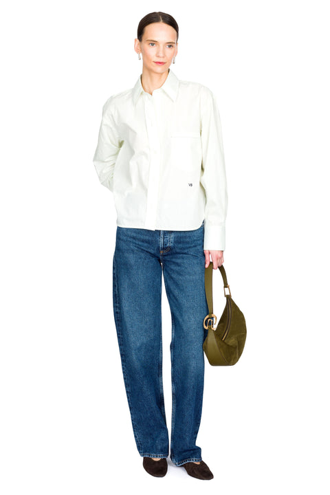 Woman posing wearing a light green button down shirt and blue jeans holding a green bag on a white background