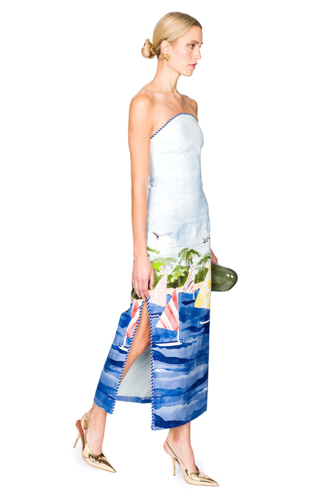 Woman walking to the right wearing a strapless dress with a colorful sailboat scene pattern on a white background