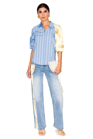Woman wears blue stripe shirt with one yellow sleeve and jeans.