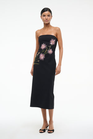 Woman wearing black, strapless midi dress that features pink dahlia embellishments across the bodice, paired with black heels.