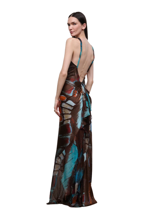 A woman modeling a floor-length backless maxi dress with a brown abstract print and teal, orange, and white accents, shown from the back against a plain white background.