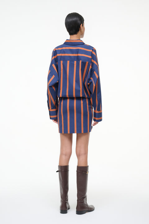Back-facing woman wearing a blue and orange striped long sleeve mini dress with brown boots.