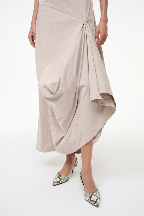 Close up of a woman wearing a beige asymmetrically draped maxi dress.