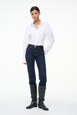 Woman wearing a white, long sleeve, button down shirt that features a tailored fit in the waist, paired with jeans and boots.