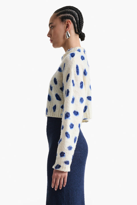 Woman faces the left in cropped kiss printed sweater.