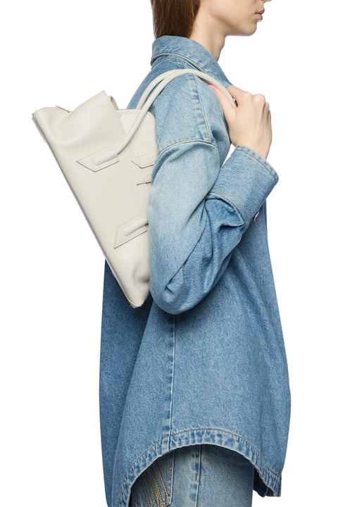 Person wearing a light blue denim jacket holding a white leather shoulder handbag.