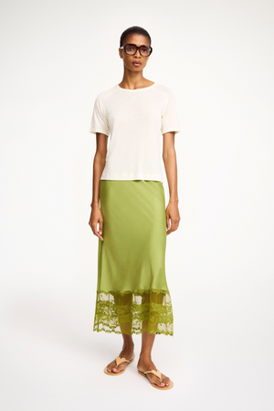 Woman wearing a white top and green skirt with lace hem on a white background