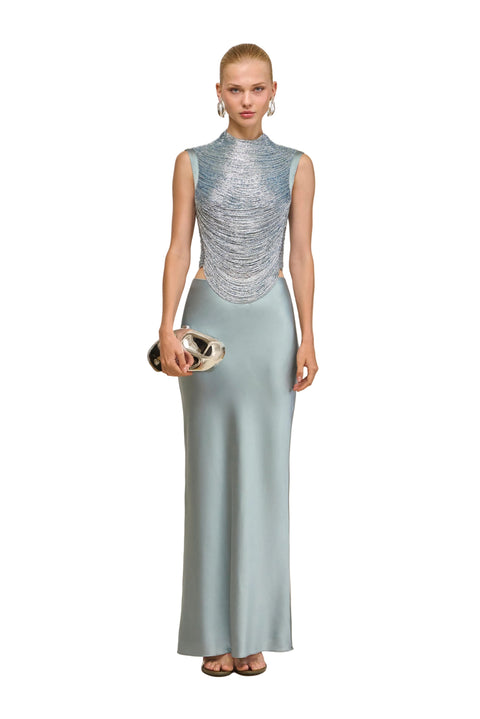 Woman wearing a blue draped sequin top and light blue skirt against a beige background