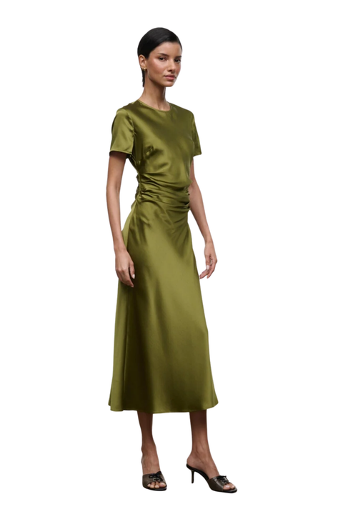 A woman modeling a short-sleeved olive green midi dress with gathered detailing at the waist, paired with dark brown heeled sandals, against a plain white background.