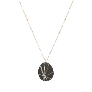A black stone stone that features white streaks, accented by streaks of small round diamonds, suspended on a yellow gold paperclip chain.