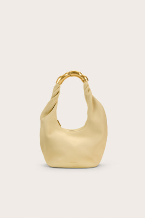 A pale yellow, leather top handle bag that features an abstract go9ld-toned handle.