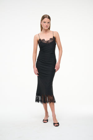 Woman wearing a black midi slip dress that features black lace trim on the neckline and hem, paired with black kitten heels.
