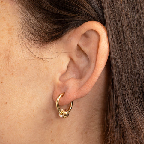 Side-facing woman wearing a small, yellow gold hoop earring with three yellow gold annulets, one pave with white diamonds.