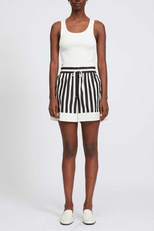 Woman wears black and white striped boxer shorts with drawstring and white tank top.