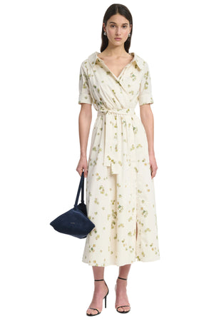 Woman wearing a beige floral dress holding a blue bag on a white background