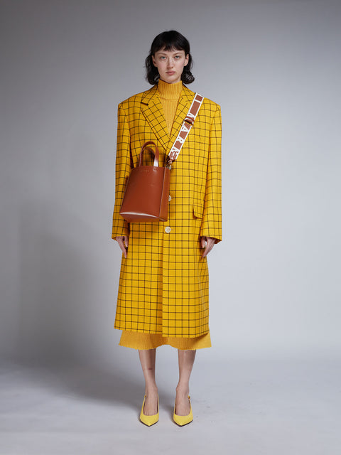 Woman wearing a yellow checkered outfit with a brown bag against a gray background