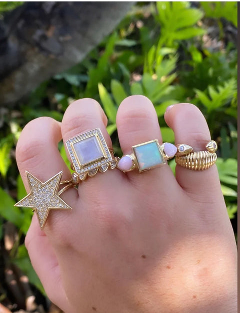 Hand wearing multiple gold rings with different designs against a blurred green background
