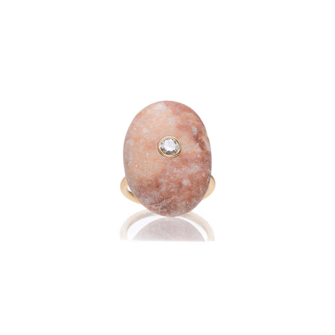 A large pink stone set embellished with a round diamond in the middle set on a yellow gold ring band.