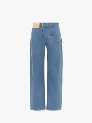Blue jeans with twisted waist and leather logo patch on front on a white background