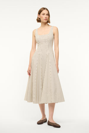 Woman wearing a midi dress that boasts a square neck, corset-style bodice, full, and full A-line skirt in a cream and brown micro stripe pattern, paired with flats.