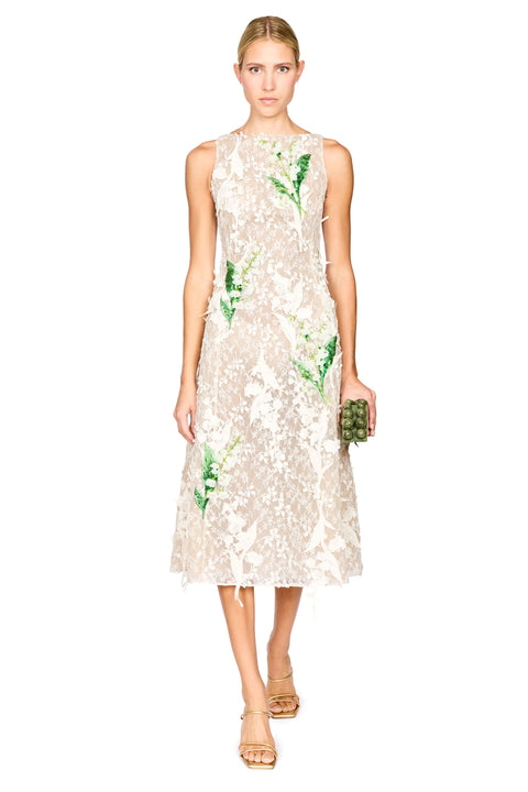 A model wearing a sleeveless cream lace midi dress with green floral applique, paired with gold high-heeled sandals, against a plain white background.