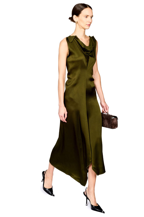 A woman modeling a sleeveless olive green satin midi dress with a draped cowl neckline, paired with black pointed-toe heels and a small brown handbag, set against a plain white background.