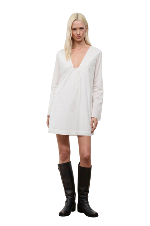 A woman wearing a low cut, long sleeve white mini dress