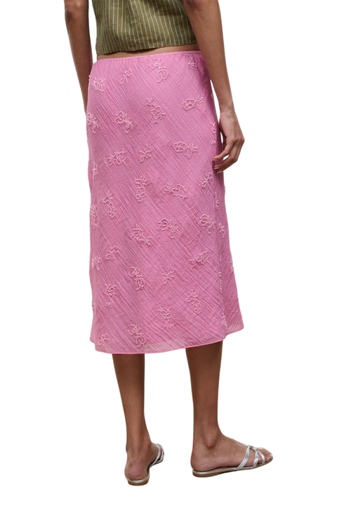 A woman wearing a pink midi skirt with beaded embellishments and a drawstring waist
