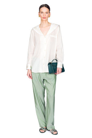 Woman wearing a white blouse and green striped pants holding a blue handbag on a white background