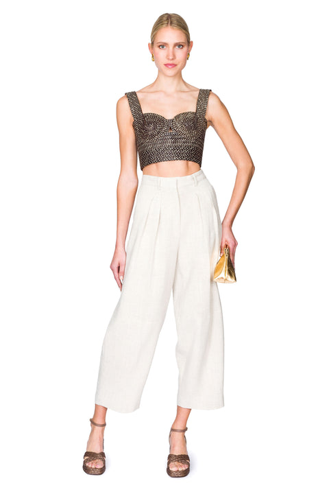 Woman posing to the side wearing a black and tan woven bustier crop top and white pants on a white background