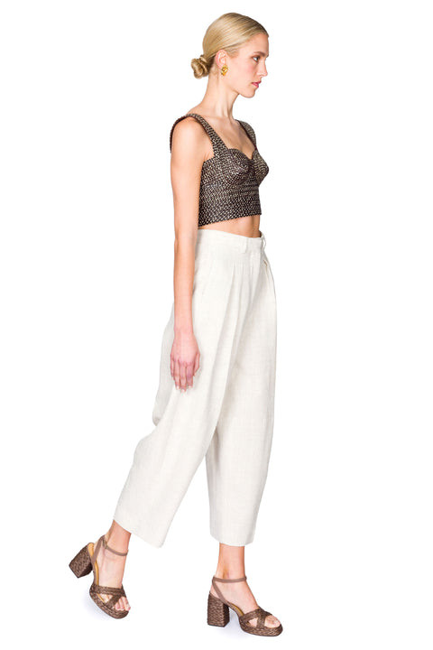 Side view of woman wearing a black and tan woven bustier crop top and white pants on a white background