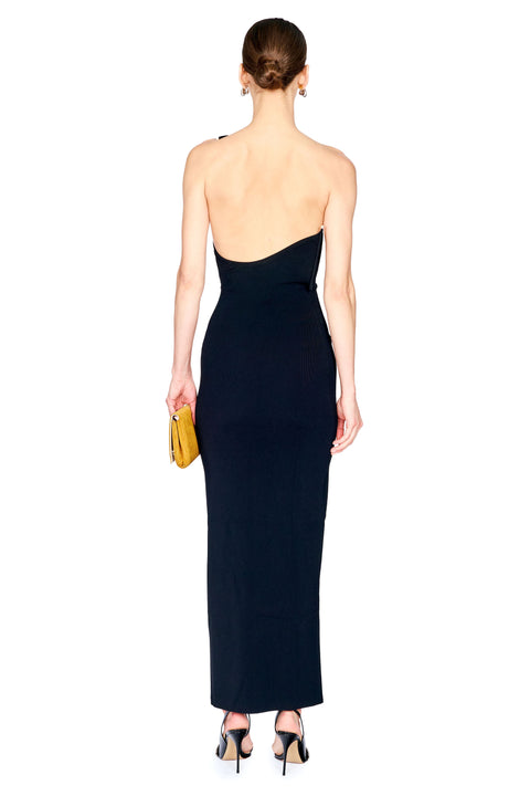 A woman shown from the back wearing a structural, one-shoulder black maxi dress with a low open back, holding a small yellow clutch and wearing black high heels against a plain white background.