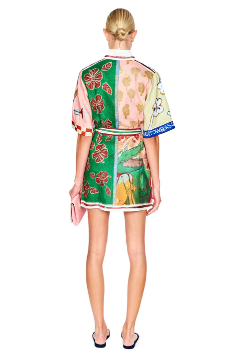 A model shown from the back wearing a short-sleeved mini dress with a vibrant multicolor patchwork print. The dress features panels of green, pink, yellow, and white with floral and animal motifs.