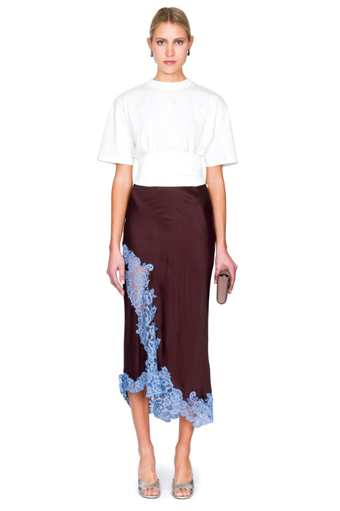 Woman posing wearing a white tuxedo t-shirt and brown skirt with blue lace details on a white background