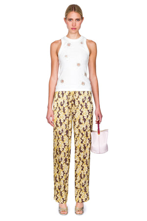 Woman wearing a white embellished top with circular cutouts and pajama style yellow pants with ornate shapes.