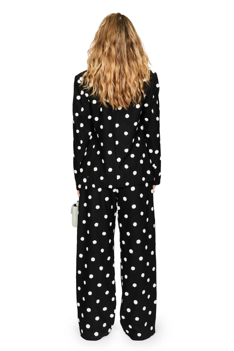 A woman viewed from behind wearing a black long-sleeve jumpsuit with a white polka dot pattern, set against a plain white background.