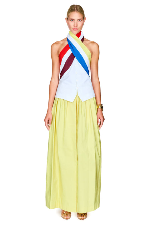 A model wearing a sleeveless halter top with diagonal red, yellow, blue, and white stripes, paired with a flowing pale yellow skirt.