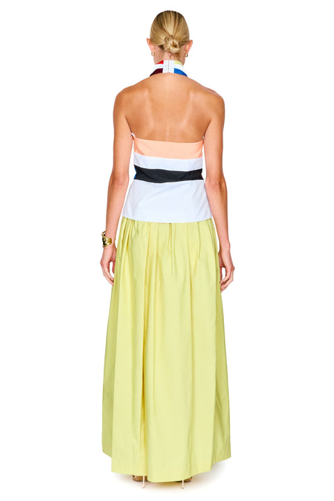 A woman shown from the back wearing a sleeveless halter top with diagonal red, yellow, blue, and white stripes, paired with a flowing pale yellow skirt.