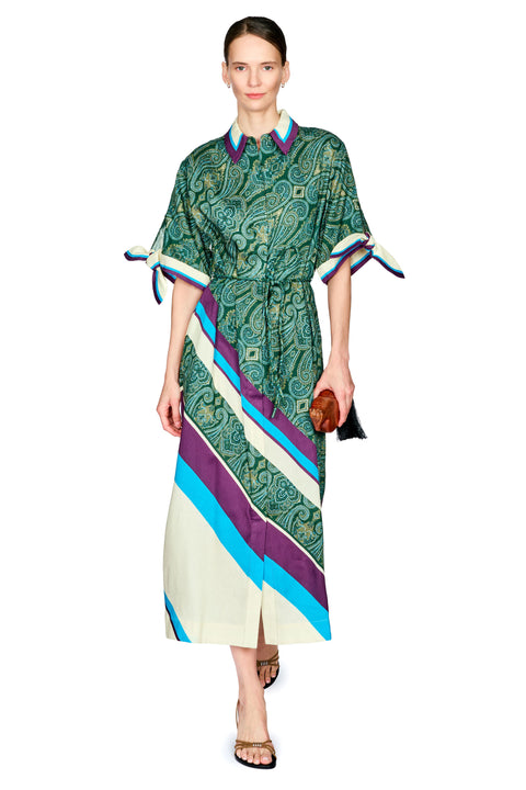 A model wearing a green and teal paisley print midi dress with diagonal cream, blue, and purple stripes on the lower half, styled with a cream shirt and brown sandals against a white background.