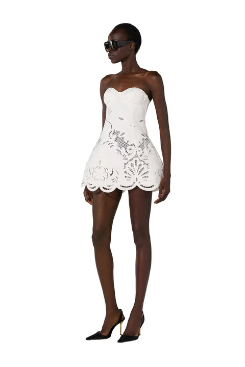 Woman wearing a white strapless dress with floral lace details on a white background