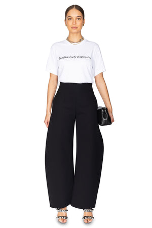 Women wears white graphic tee with black wide leg pants and black clutch.