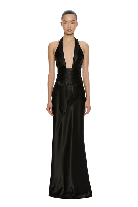 A model wearing a floor-length black satin halter gown with a deep plunging neckline and a matching waist sash, photographed against a solid white background.