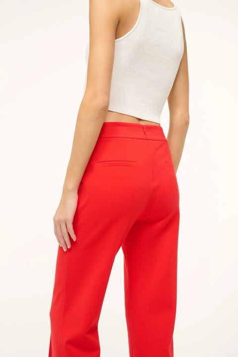 Close up back-facing woman wearing bright red crop flare pants with a front center seam, paired with a white tank. 