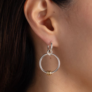 A woman wearing Spinelli Kilcollin Asha earrings that feature three linked sterling silver hoops with three yellow gold annulets. 