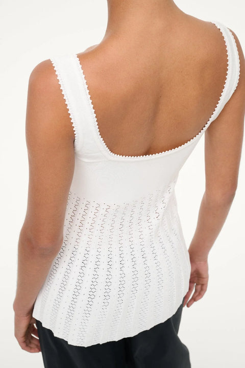 Back view of a woman wearing a white knit tank top that features a scoop back and sheer, pleated bodice, paired with black bottoms. 
