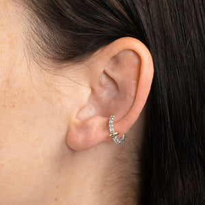 Woman wearing a sterling silver ear cuff pave with grey diamonds featuring a yellow gold annulet. 