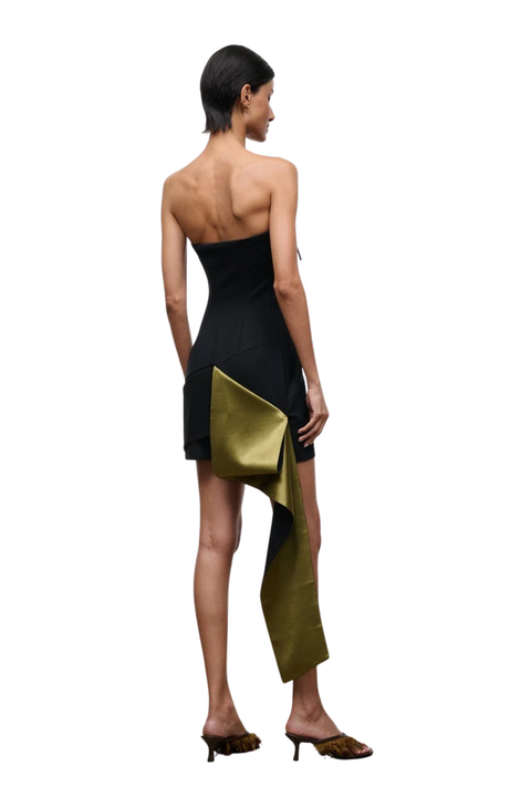 A model shown from the back wearing a strapless black dress with a draped olive green fabric panel and matching brown heels, set against a plain white background.