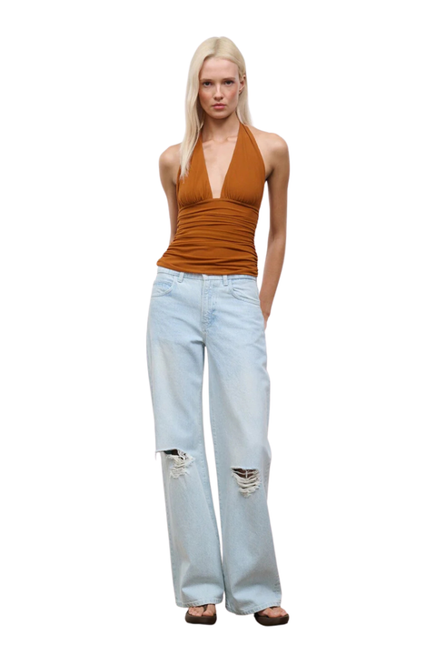 A blonde model wearing a rust-brown halter top and light-wash distressed wide-leg jeans, standing against a plain white background.