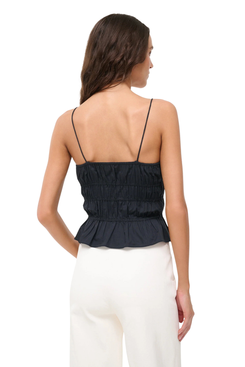 A woman shown from the back wearing a black smocked camisole top with thin spaghetti straps and white pants, against a plain white background.